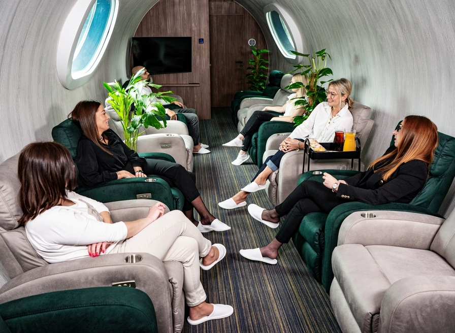 Cozy relaxation lounge with plush recliners, large round windows, and guests wearing slippers enjoying a calm conversation.