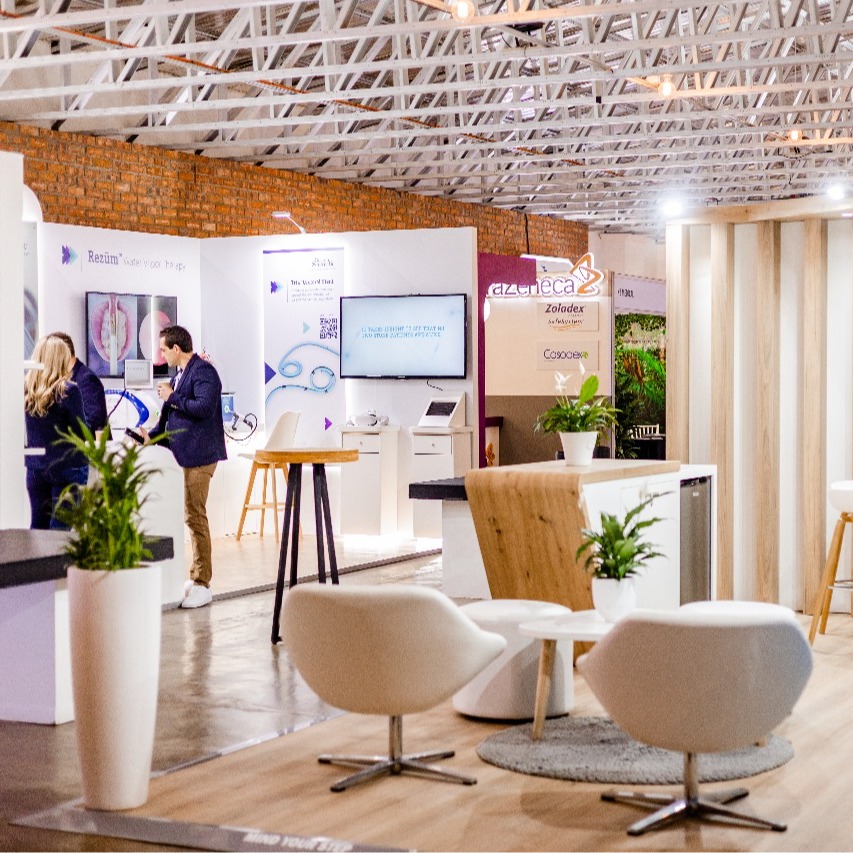 Contemporary hotel lounge and networking area with white swivel chairs, high stools, potted plants and exhibition booths