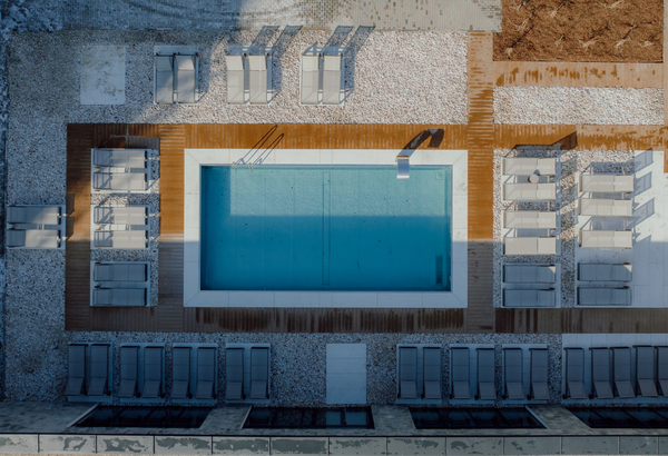 Nowoczesny basen hotelowy otoczony drewnianym tarasem i licznymi leżakami na kamiennym podłożu.