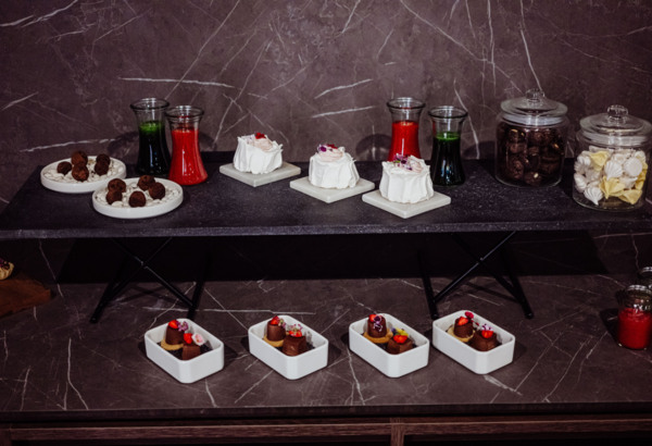 Eleganckie desery i napoje na marmurowym stole, z mini tortami, truflami, ciasteczkami i owocowymi sokami.