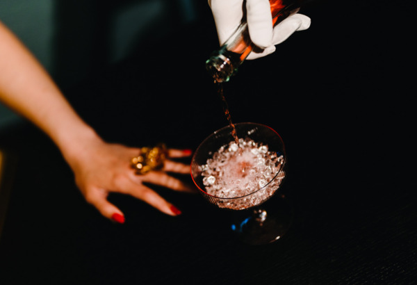 Wykwintny trunek nalewany do kieliszka z lodem na eleganckim barze, w otoczeniu nocnej atmosfery.