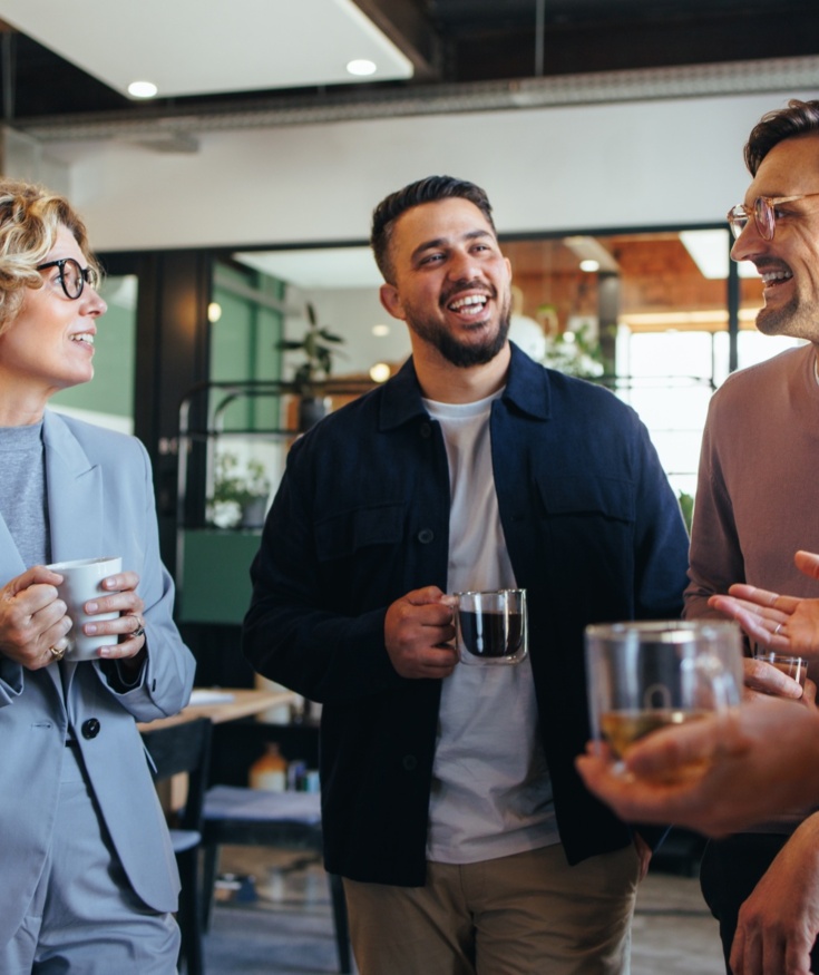Cztery osoby rozmawiają i piją kawę w nowoczesnej sali konferencyjnej hotelu z jasnym oświetleniem i drewnianym stołem.