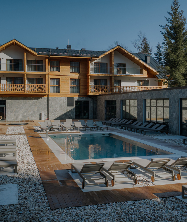 Nowoczesny hotel z drewnianymi balkonami, kamiennym patio i basenem otoczonym leżakami do relaksu na zewnątrz.