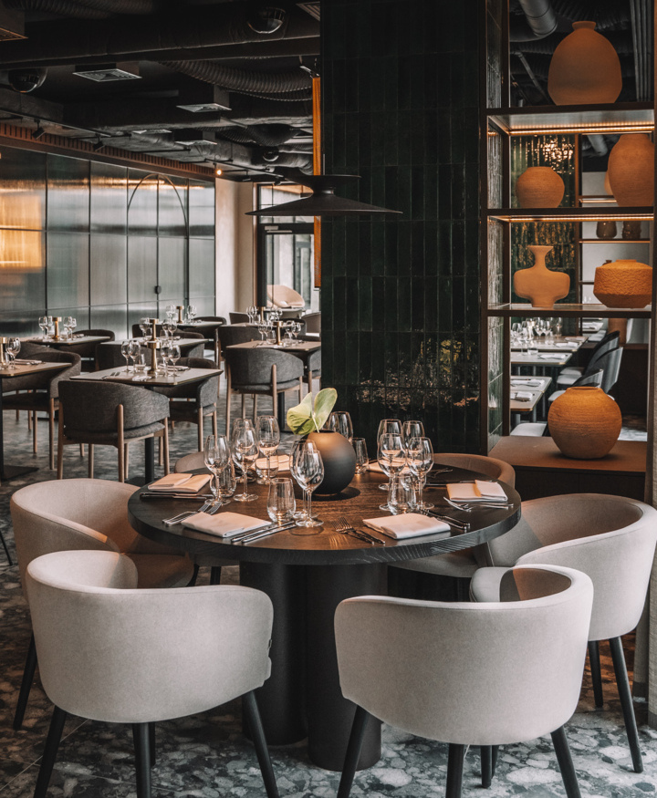 Elegancka restauracja z okrągłym stołem, miękkimi fotelami i subtelną dekoracją na przytulnej marmurowej podłodze.