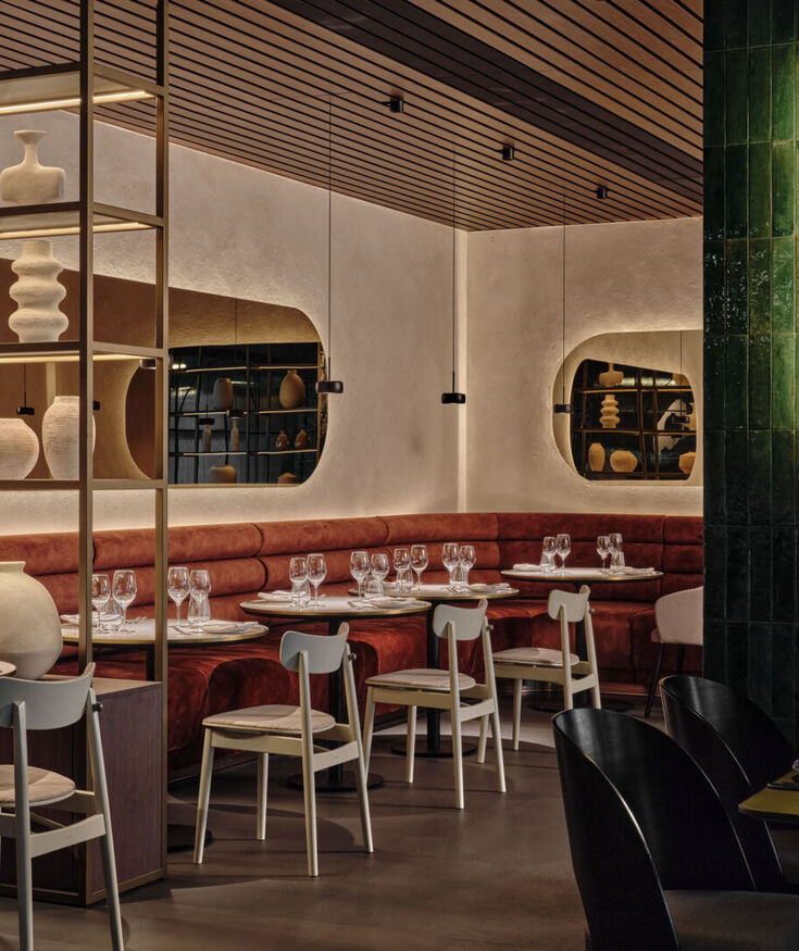 Elegancka restauracja z miękkimi, bordowymi sofami, białymi krzesłami i dekoracyjnymi ceramikami w nowoczesnym wnętrzu.