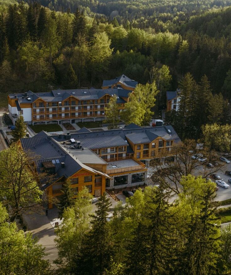 Hotel w otoczeniu gęstego lasu z drewnianą elewacją, wielopiętrowy z parkingiem i spokojną, zieloną okolicą.