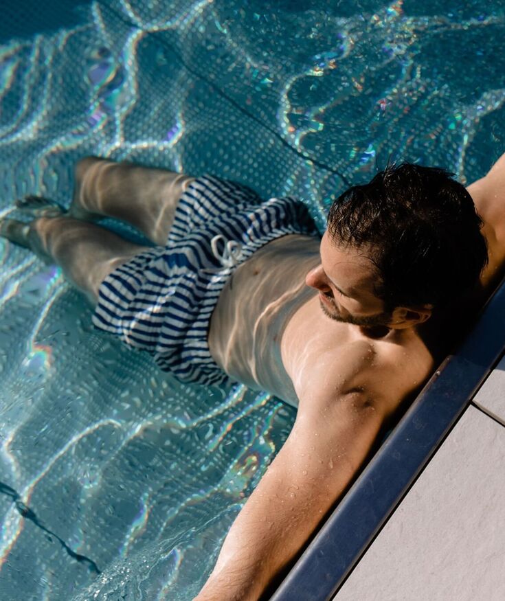 Mężczyzna relaksuje się w basenie hotelowym, opierając się o krawędź i ciesząc się słońcem i wodą