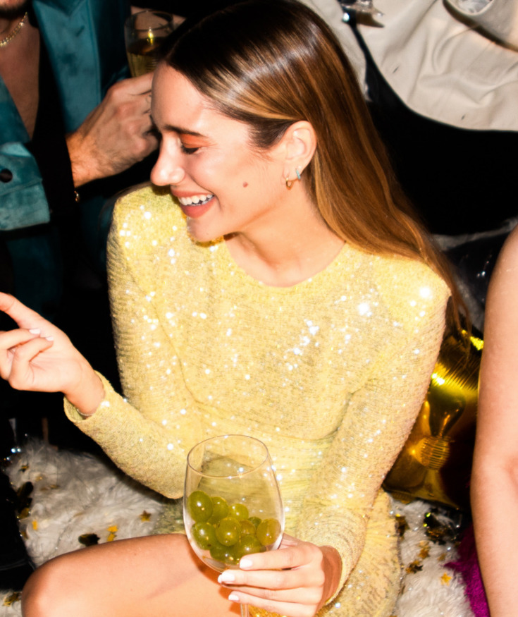 Goście bawią się podczas wieczornej imprezy w eleganckim otoczeniu, jedna kobieta trzyma kieliszek z zielonymi winogronami.