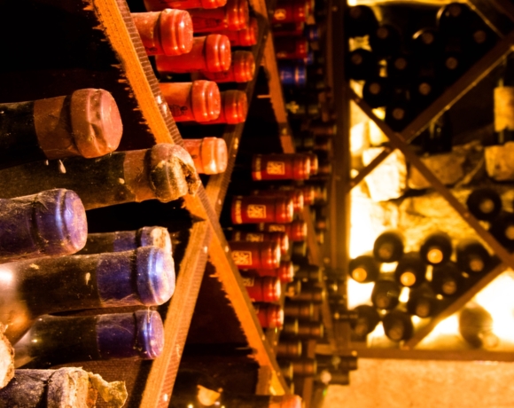 Rustiikkinen viinikellari, jossa pölyisiä pulloja vaakatasossa puisilla hyllyillä lämpimässä valossa