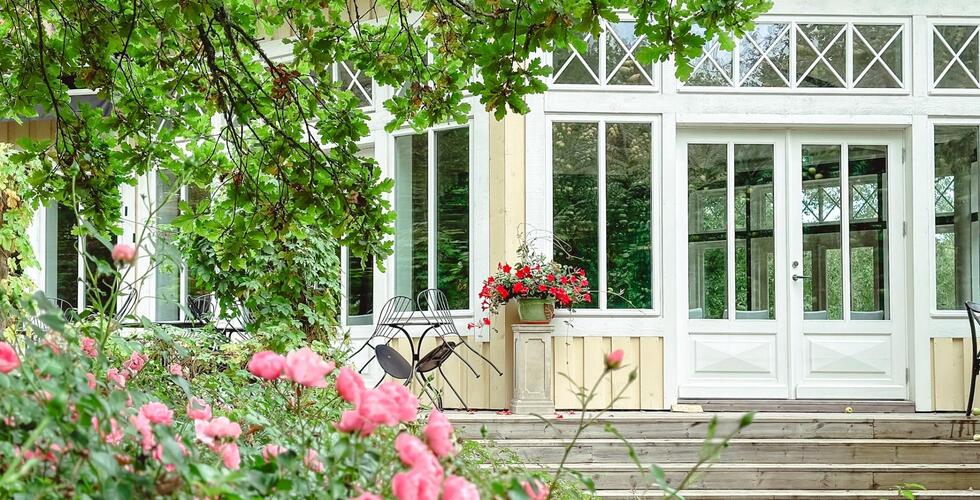 Viehättävä hotellin puutarhaterassi vanhoine tuoleineen, kirkkaan vaaleanpunaisine ruusuineen ja suurine valkoisin kehyksin varustettuine ikkunoineen