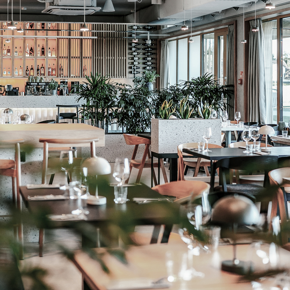 Nowoczesna restauracja hotelowa z marmurowym barem, podświetlonymi półkami z alkoholem, roślinami i nakrytymi stołami