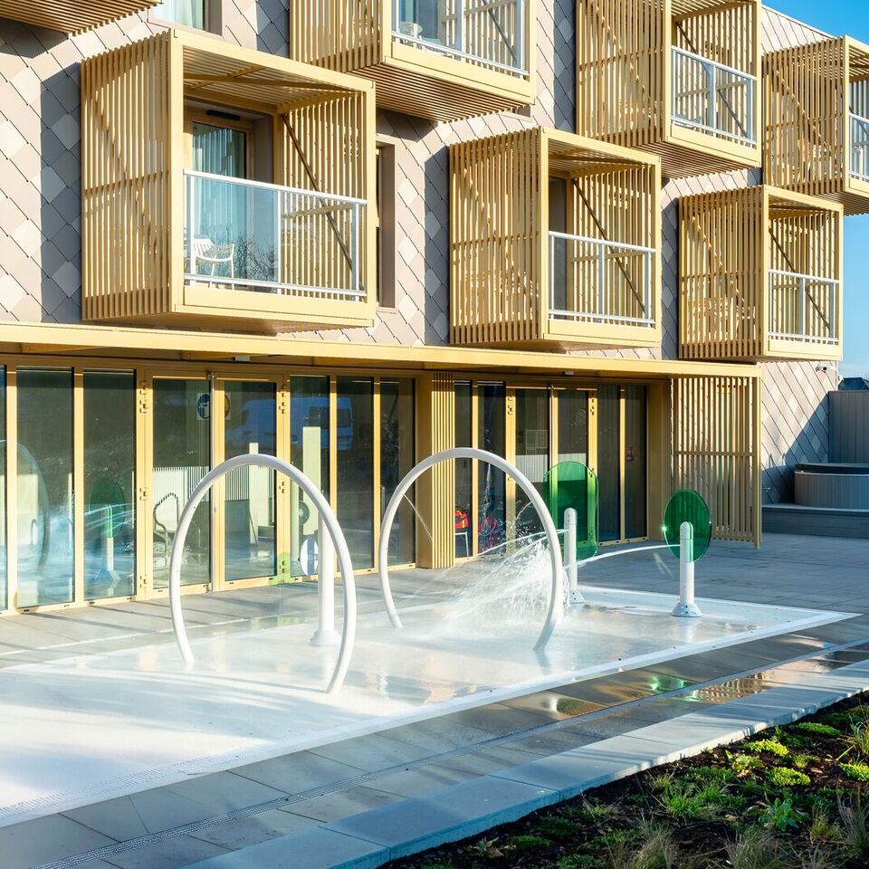 Słoneczne patio hotelowe z płytkim brodzikiem i wodnymi łukami, prywatne drewniane balkony oraz zewnętrzne jacuzzi.