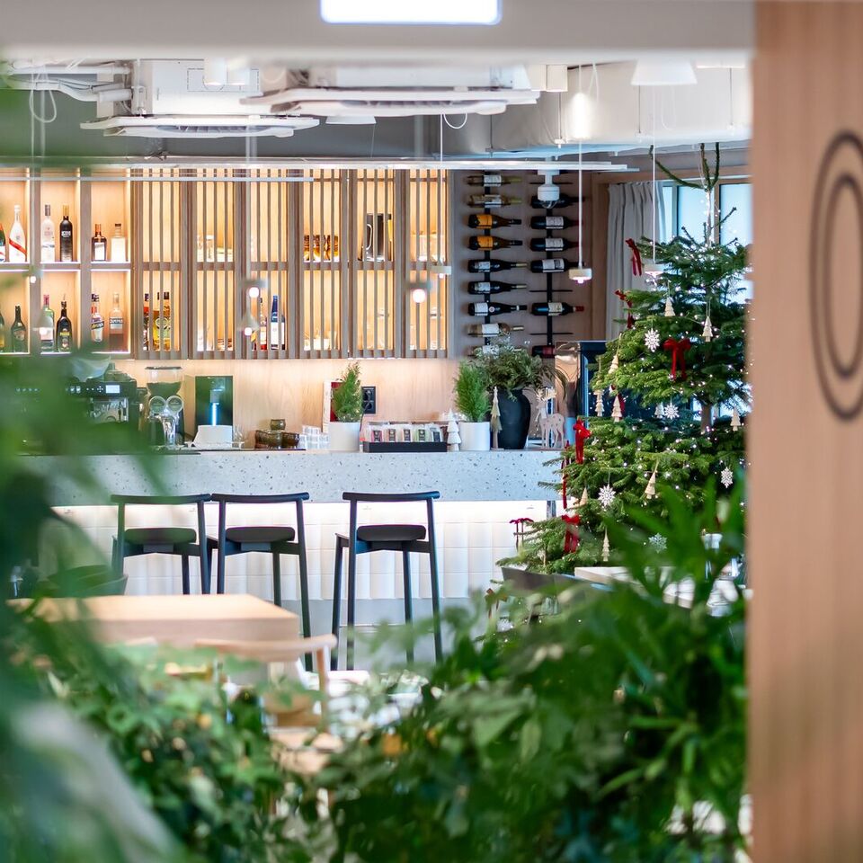 Nowoczesny bar hotelowy z podświetlonymi półkami na alkohole, blatem terrazzo, wysokimi stołkami, choinką i zielenią