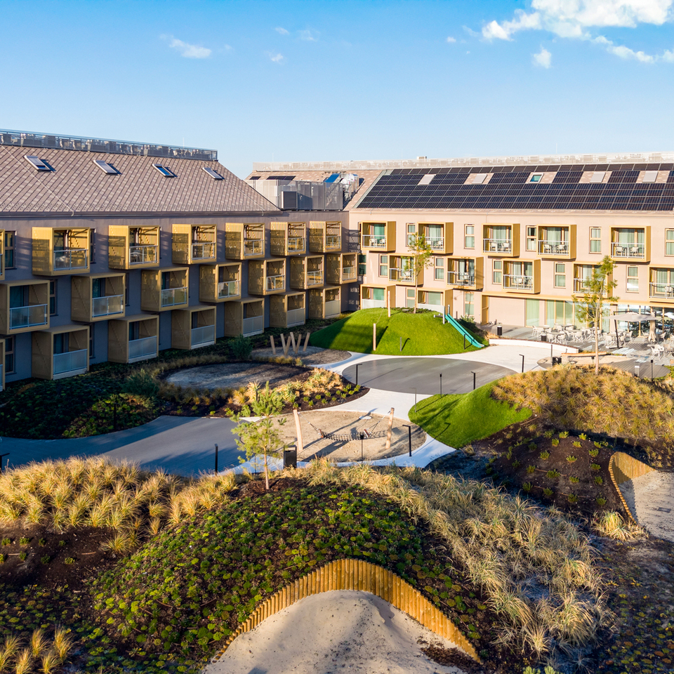 Hotel courtyard with private balconies, solar panels on roof, landscaped mounds, outdoor dining terrace and kids' play area.