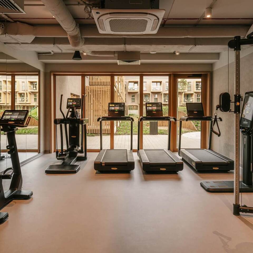 Nowoczesna sala fitness w hotelu z bieżniami, orbitrekami i sprzętem Technogym przy dużych oknach z widokiem na patio