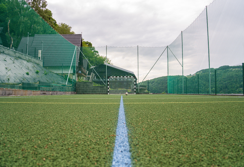 Kunstrasen-Fußballplatz mit kleinem Tor und Ball, hohen Schutznetzen und Hügelblick im Hotel-Sportbereich