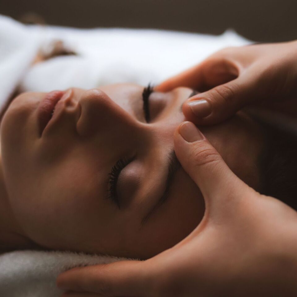 Relaksacyjny zabieg spa — gość z zamkniętymi oczami otrzymuje delikatny masaż czoła i skroni na miękkim ręczniku.