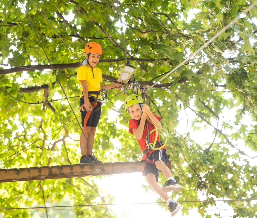 Dwójka dzieci bawiących się w parku linowym w koronach drzew – aktywna przygoda na wysokości
