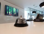 Dzwonek recepcyjny stojący na blacie, w tle widać telewizor