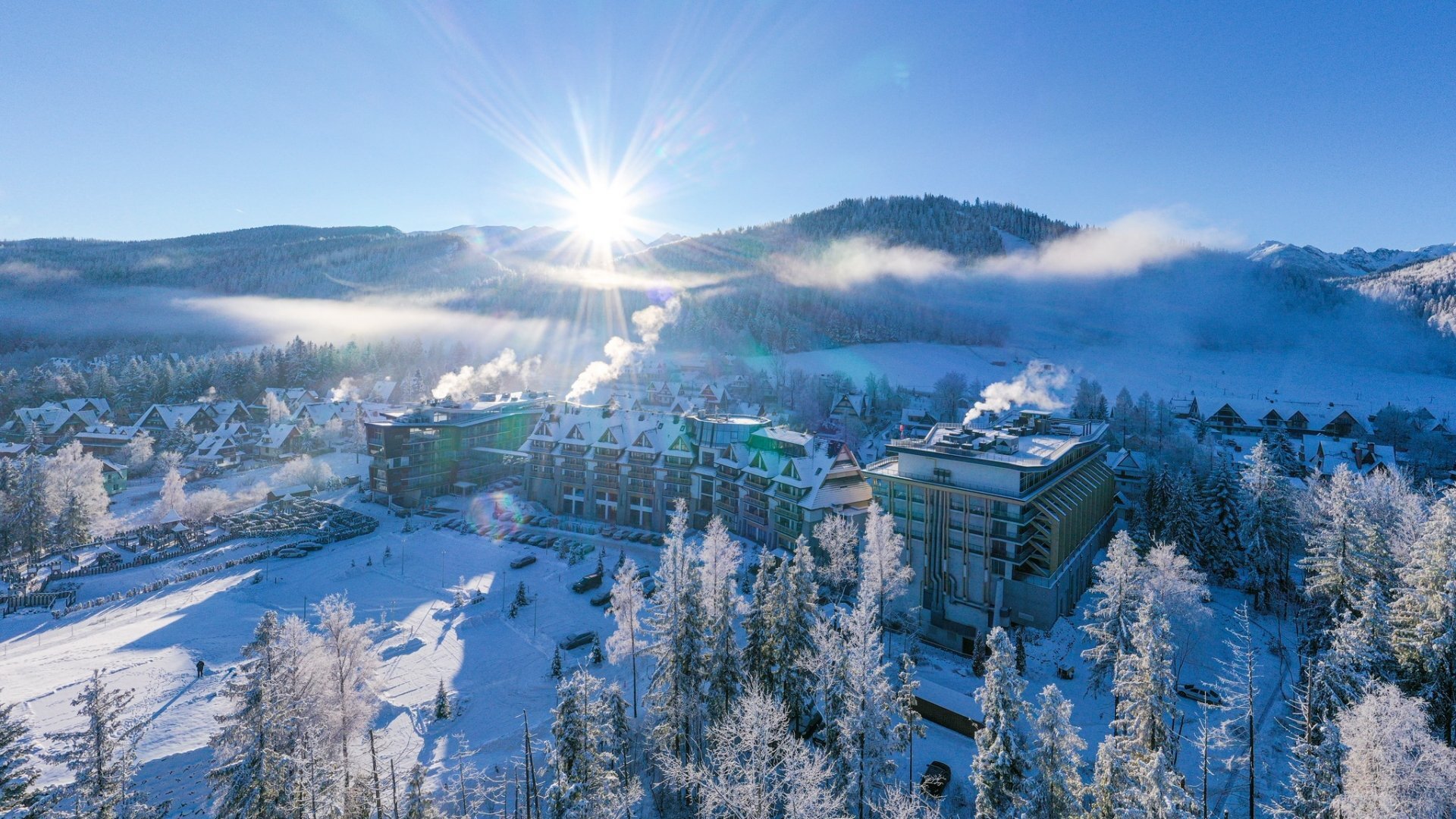 A snow-covered hotel in the mountains seen from a bird's eye view, with a panorama of the mountains