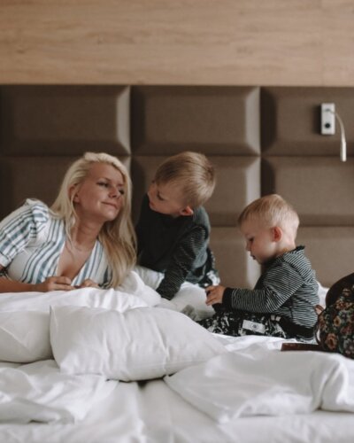 Mama z dziećmi spędzająca czas w przytulnym pokoju hotelowym z dużym łóżkiem