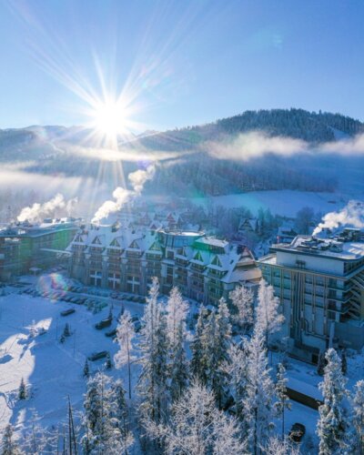 Ośnieżony hotel w górach widziany z lotu ptaka, z panoramą Tatr i promieniami słońca nad szczytami