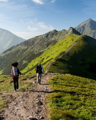 Ludzie podczas pieszej wędrówki górskim szlakiem wśród zielonych wzgórz