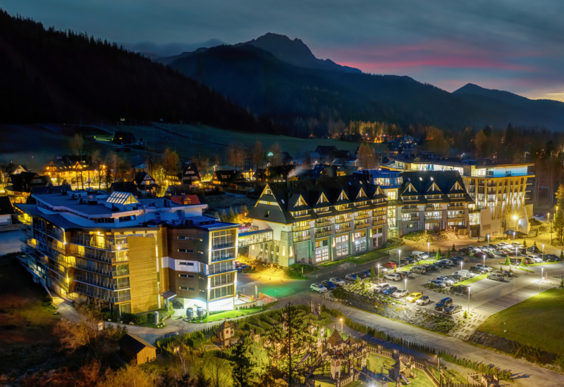 Osvetlená, moderná hotelová budova Nosalowy Dwór s výhľadom na hory a viditeľným parkoviskom