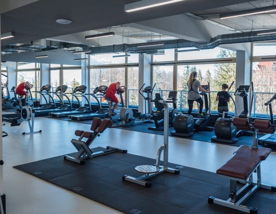 People training on exercise bikes and elliptical trainers in a modern gym with a view