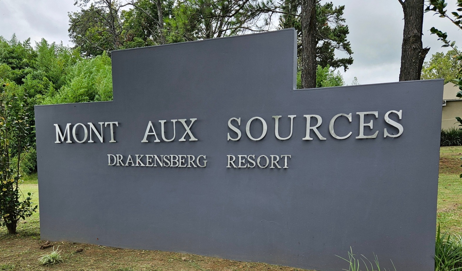Mont Aux Sources Drakensberg Resort gray entrance sign on manicured lawn, framed by pine trees and greenery