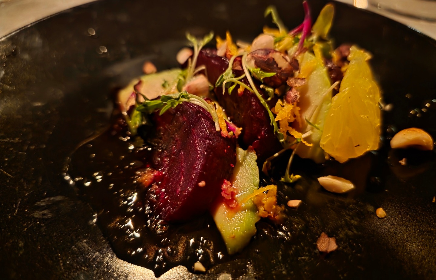 Roasted beet and citrus salad with apple slices, microgreens and crushed nuts on a glossy black plate
