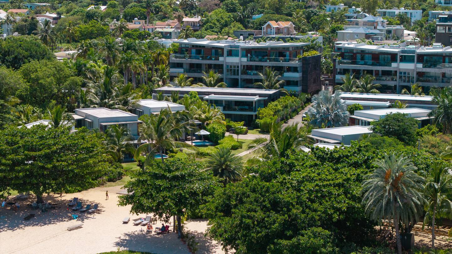 Beachfront resort with modern low-rise villas and condos amid palms, private plunge pools, sandy beach with loungers