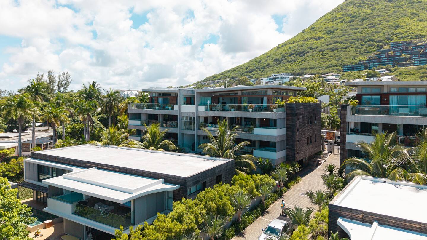 Modern beachfront resort with multi-level suites, glass balconies and private terraces, palm-lined paths and lush hillside views.