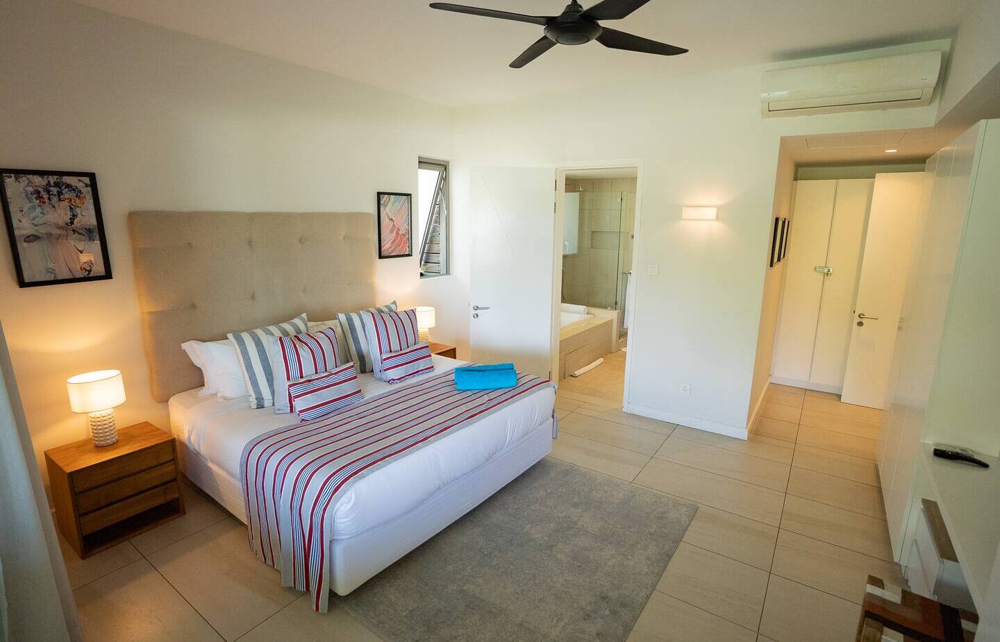 Bright modern king room with tufted headboard, striped bedding, bedside lamps, ceiling fan, AC and en-suite bathtub.