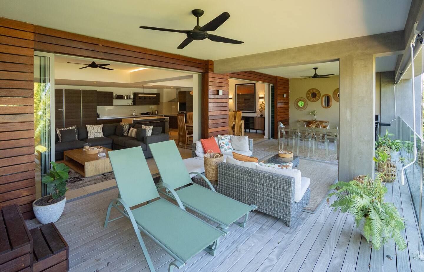 Open-plan terrace with two loungers, wicker sofa, alfresco dining, modern kitchen, ceiling fans and potted plants