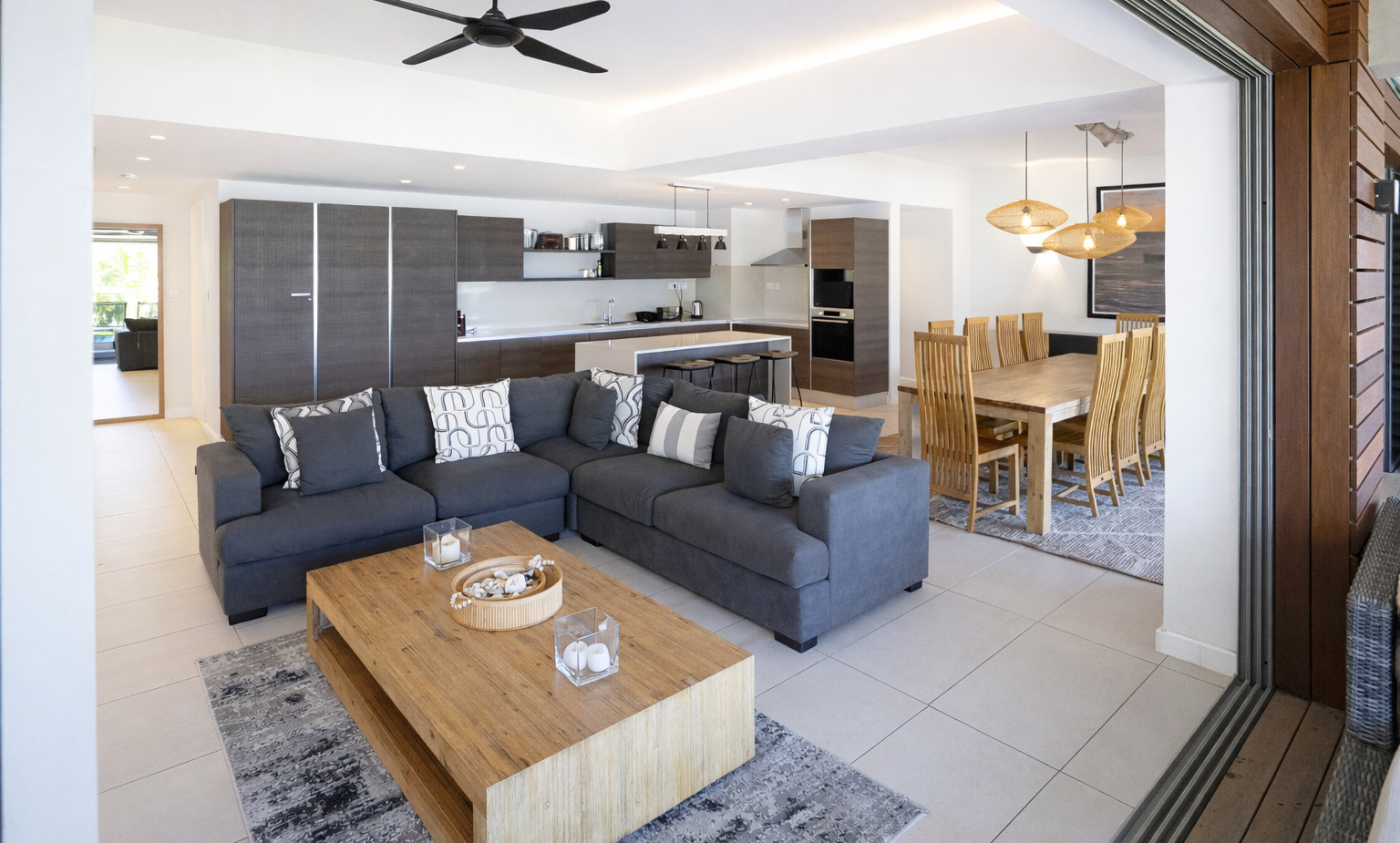 Open-plan living with gray sectional, wooden table, island with stools, dining for 8 and sliding terrace doors.