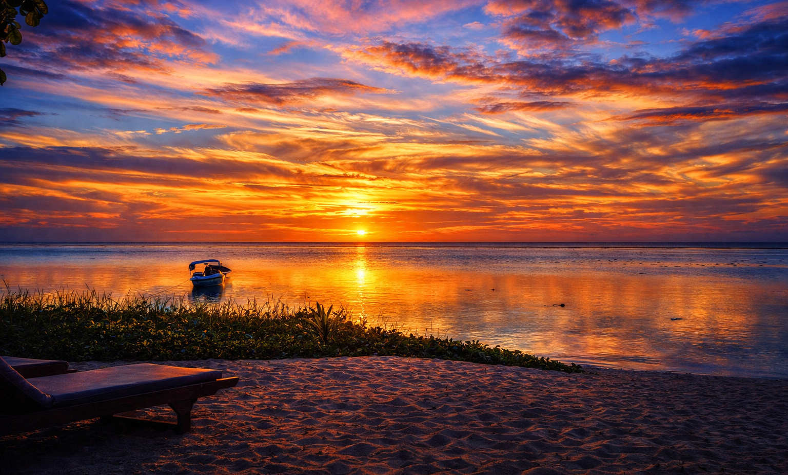 Two wooden sun loungers on sandy beachfront, small boat on calm water, vivid orange and purple sunset reflecting on the sea