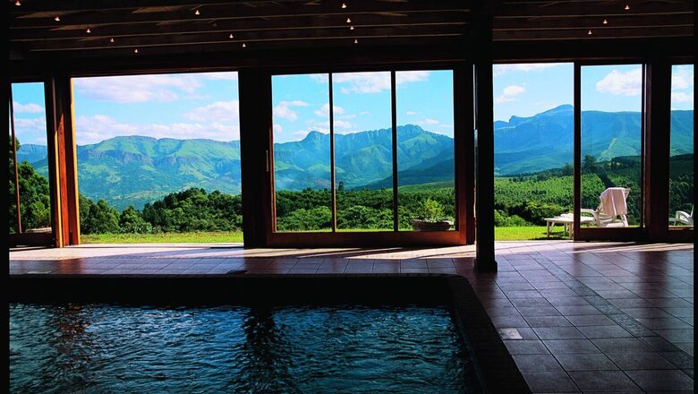 Indoor pool at Mont Coach House Hotel & Spa, with tiled deck, wooden beams, floor-to-ceiling glass doors, lounge chairs, lawn views and mountain vistas.
