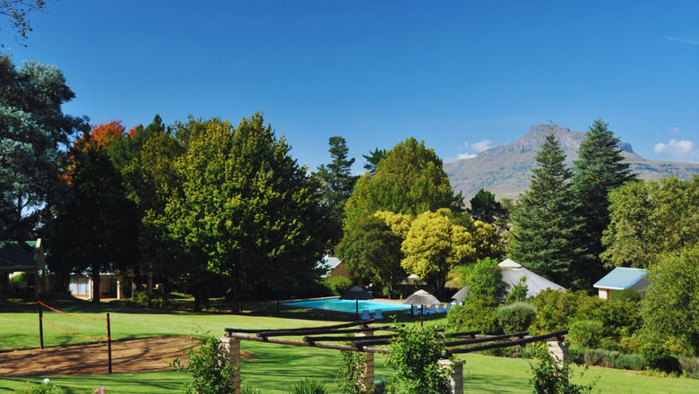Lush gardens at Mont Aux Sources Drakensberg Resort, featuring an outdoor chess set, pergola, sunlit lawn, swimming pool and cottages with mountain views in the Northern Drakensberg.