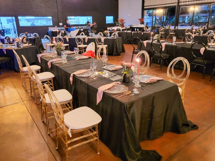 Elegant indoor banquet with black linens, ghost chairs, pink napkins, candlelit place settings and floral centerpieces.