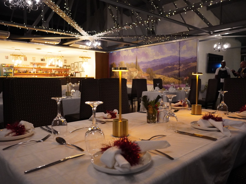 Elegant hotel dining room with warm tabletop lamps, white linens, set places, twinkling ceiling lights and painted mural