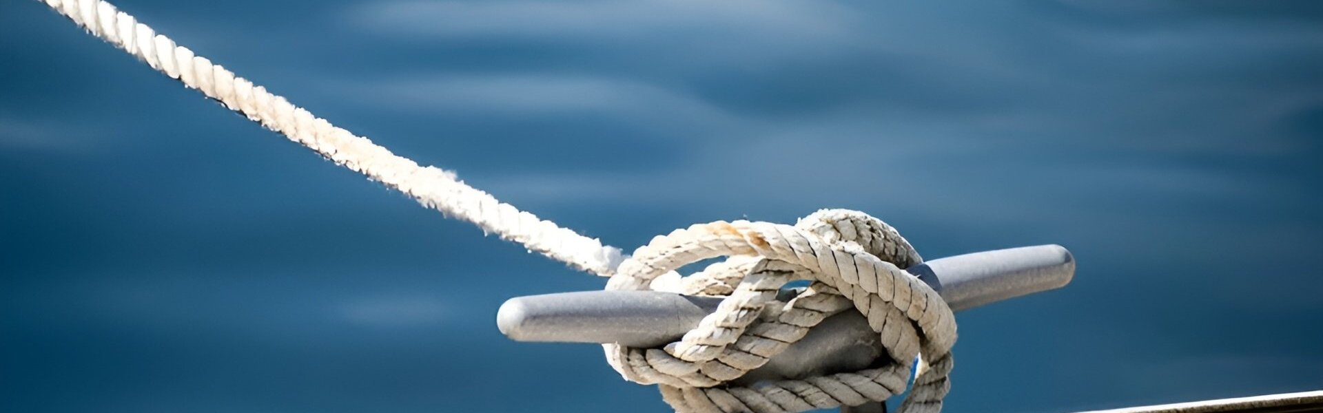 Thick mooring ropes tied around a cleat on a dock above calm blue water