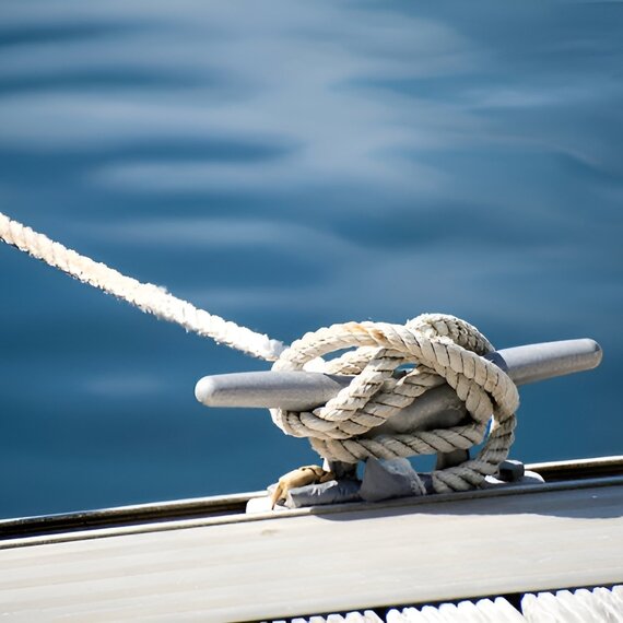 Thick mooring ropes tied around a cleat on a dock above calm blue water