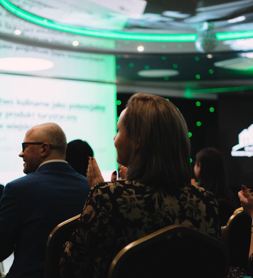 Guests seated in hotel conference room applauding during a presentation with modern LED lighting in the background