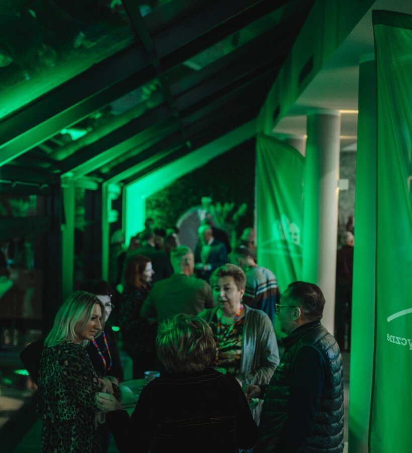 Guests socialize in a cozy, green-lit hotel lobby during an evening social event with modern architectural design.