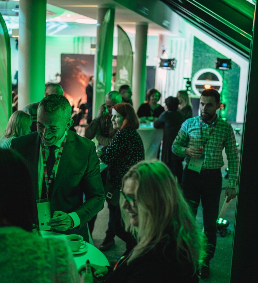 People networking at a modern conference room event with green lighting and casual conversations