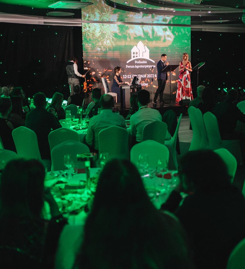 Conference room with tables and chairs set, musicians performing on stage, guests seated enjoying the agrotourism forum event.