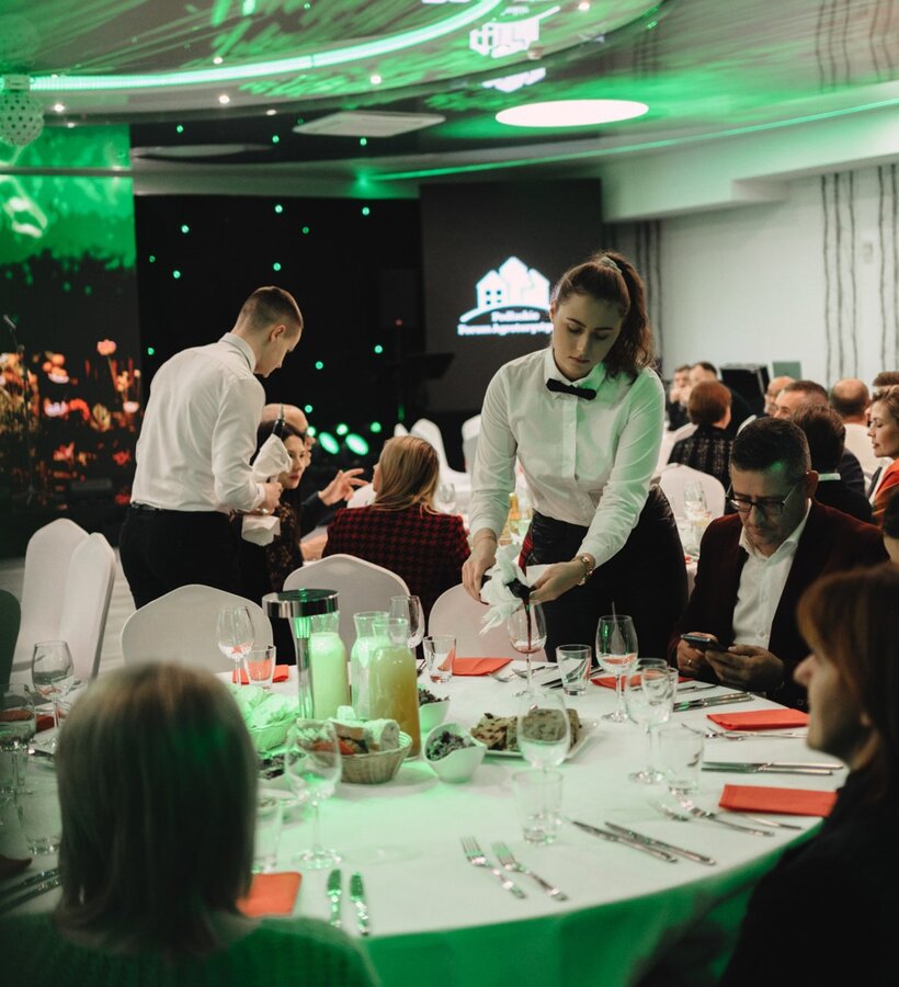 Elegant business dinner with white tablecloths, attentive waitstaff, and glassware set on tables in a modern conference room