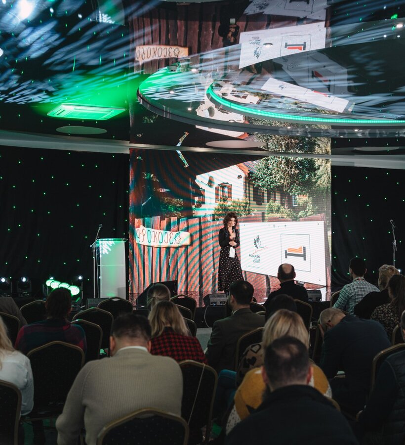 Conference room with a speaker addressing the audience at a modern hotel event with LED screens and stage lighting