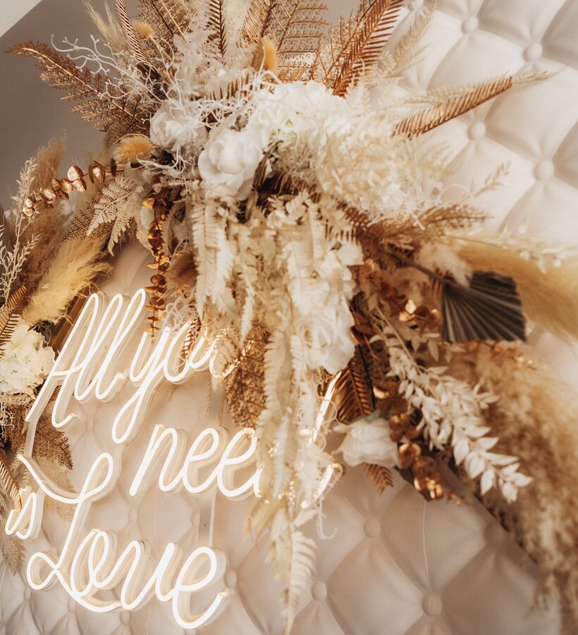 Wall decoration with soft beige and gold foliage and neon sign 'All you need is Love' on quilted white fabric backdrop